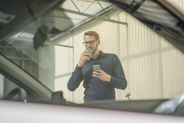 Lächelnder Geschäftsmann mit Handy und Tasse Kaffee