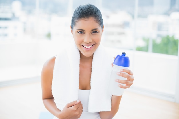 Lächelnder getonter Brunette mit dem Tuch, das Sportflasche hält