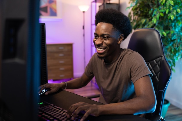 Lächelnder glücklicher Junge sitzt in einem Raum, der mit farbigen LED-Lichtern beleuchtet ist. Professioneller Gamer spielt Computer