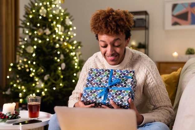 Lächelnder glücklicher Mann spricht über Laptop-Webcam mit Familie und öffnet Weihnachtsgeschenk von ihnen live