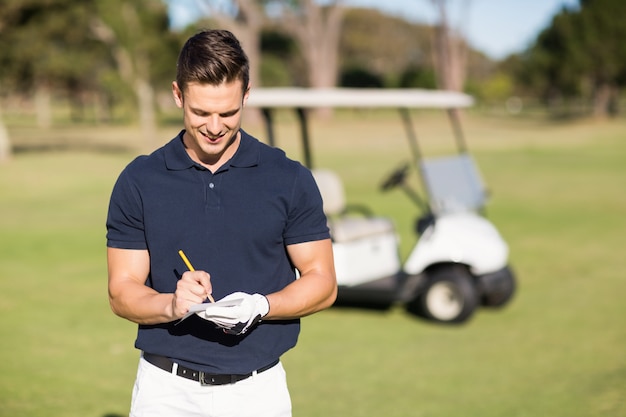 Lächelnder Golfer, der auf Scorekarte schreibt