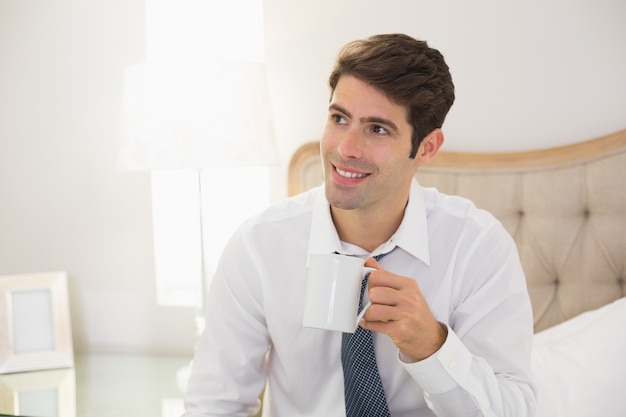 Lächelnder gut gekleideter trinkender Kaffee des Mannes im Bett