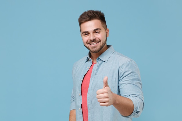 Lächelnder gutaussehender junger bärtiger Kerl der 20er Jahre im Freizeithemd posiert isoliert auf pastellblauem Wandhintergrund Studioporträt. Menschen aufrichtige Emotionen, Lifestyle-Konzept. Mock-up-Kopienbereich. Daumen nach oben zeigen.
