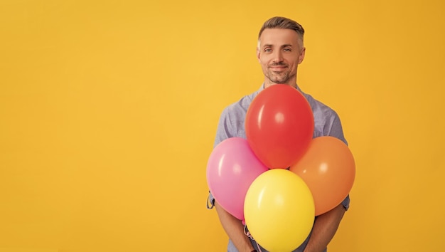 Lächelnder gutaussehender Mann hält Partyballons auf gelbem Hintergrund, Kopienraum einkaufen