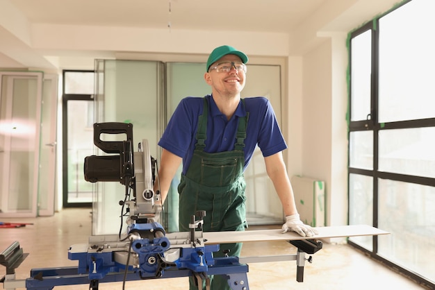 Lächelnder Handwerker mit Brille schneidet Brett mit Kreissäge in neuem Bürogebäude renovieren und