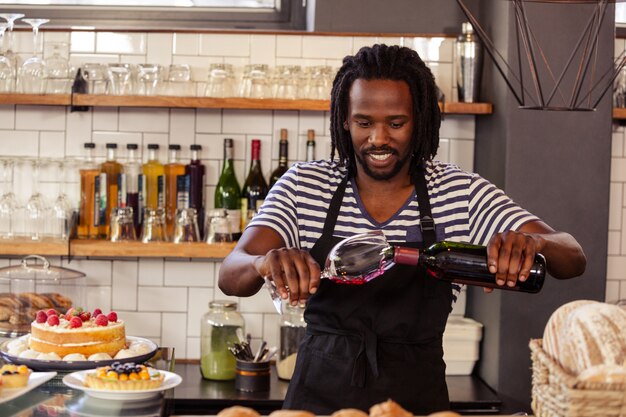 Lächelnder Hipster-Mitarbeiter, der Glas Wein füllt