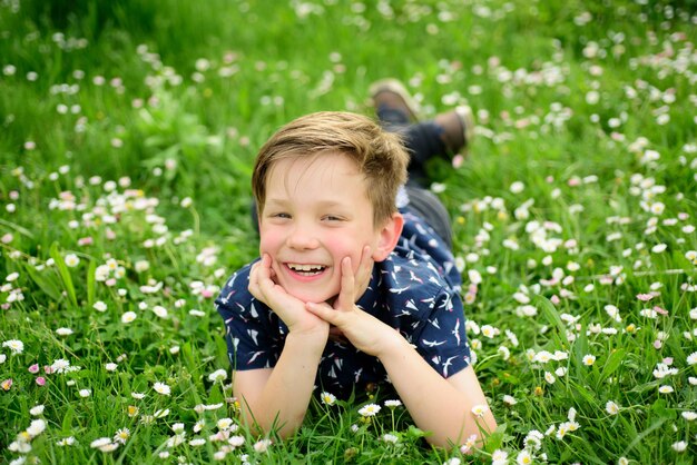 Lächelnder Junge, der auf einem sorglosen Blumenfeld liegt, süßes Kind, das auf dem Feld genießt und träumt