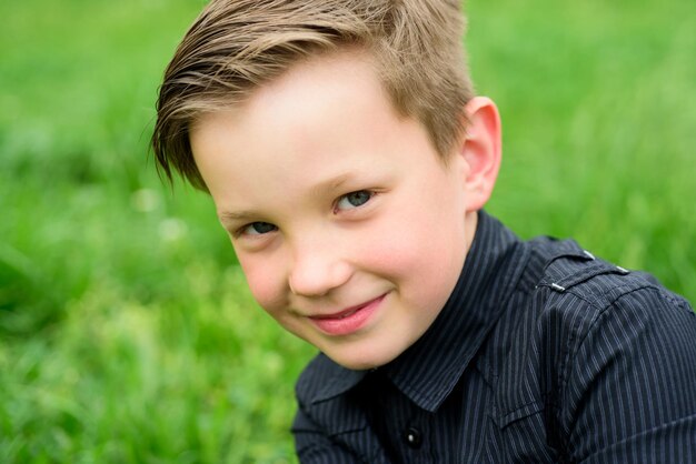 Lächelnder Junge im stilvollen schwarzen T-Shirt im Freien am Grashintergrund