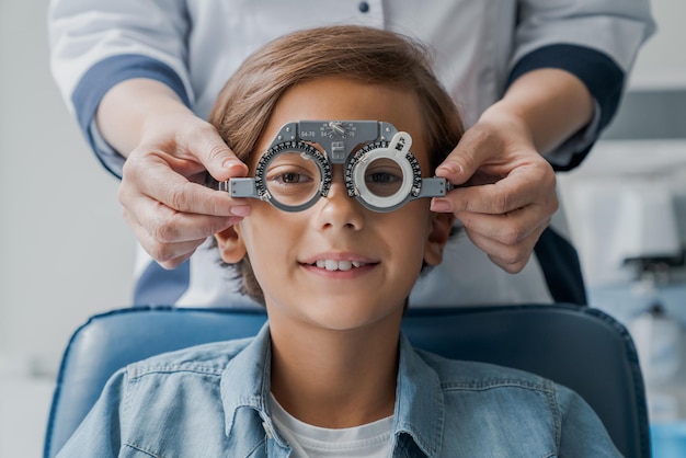 Lächelnder Junge mit Brille überprüft das Sehvermögen beim pädiatrischen Augenarzt