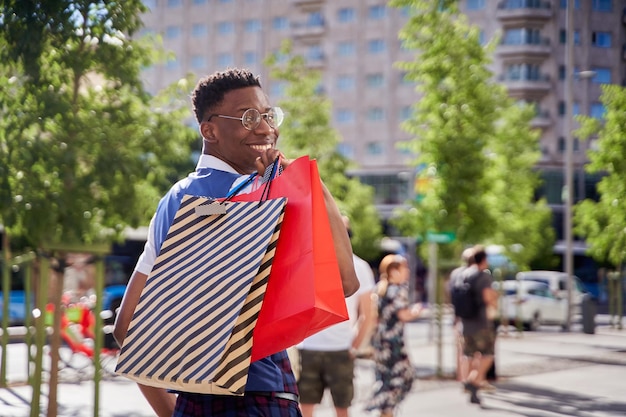 Lächelnder junger Afroamerikaner, der Einkaufstaschen trägt und in die Kamera schaut