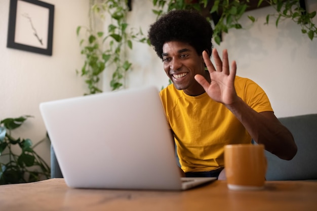 Lächelnder junger Afroamerikaner mit Laptop winken bei einem Videoanruf. Technologiekonzept.