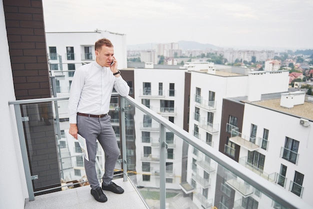 Lächelnder junger Architekt oder Ingenieurbauer in einem Hut mit Tablet über einer Gruppe von Bauherren auf einer Baustelle Architekt beobachtet ein Bauunternehmen Gebäudeindustrie Menschen Konzept