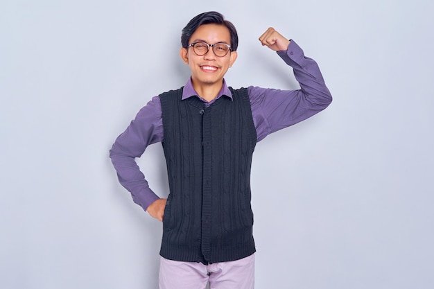 Lächelnder junger asiatischer Mann in legerem Hemd und Weste hebt die Arme und zeigt Muskeln, die auf weißem Hintergrund isoliert sind Menschen-Lifestyle-Konzept