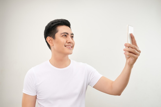 Lächelnder junger asiatischer Mann macht Selfie-Foto auf dem Smartphone auf weißem Hintergrund making