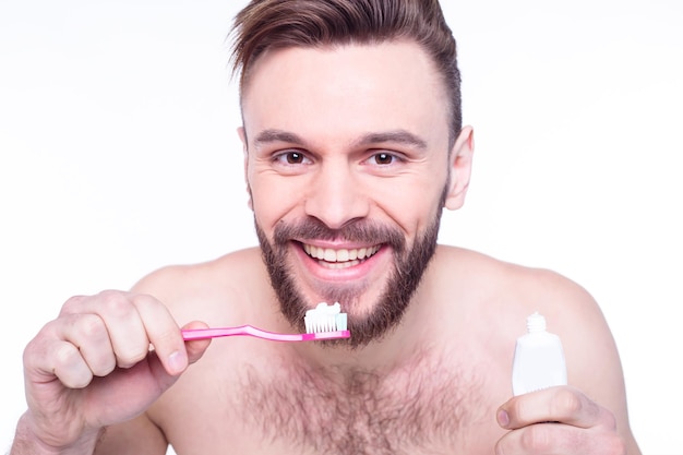 Lächelnder junger bärtiger Mann mit Zahnbürste, der die Zähne putzt und auf das Badezimmer blickt, um das Badezimmer zu spiegeln Zahnhygiene und Schönheitskonzept im Gesundheitswesen