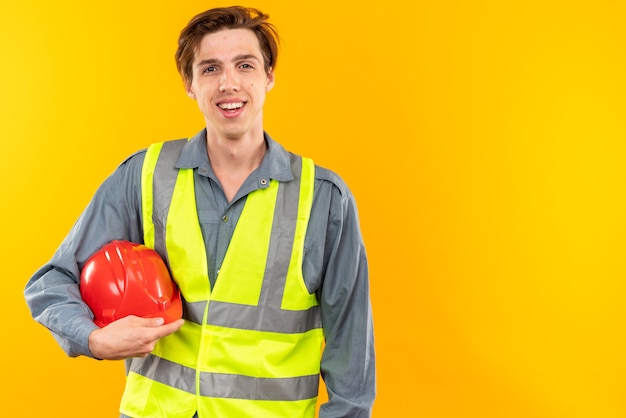 Lächelnder junger Baumeister in Uniform mit Schutzhelm mit Kopierraum
