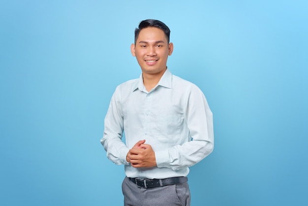 Lächelnder junger gutaussehender Geschäftsmann, der Händchen hält mit einem selbstbewussten Gesicht auf blauem Hintergrund