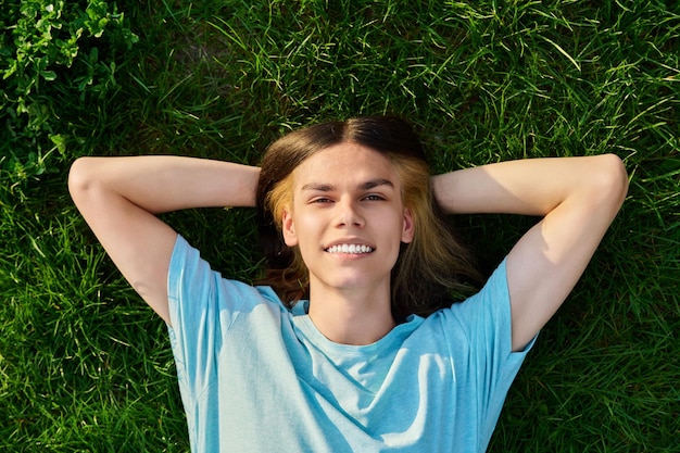Lächelnder junger Kerl, der die Kamera betrachtet, die auf dem Gras liegt