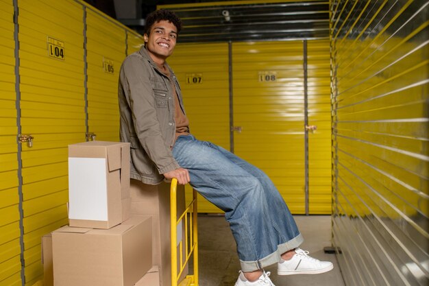 Lächelnder junger Lagerarbeiter, der auf der Kiste sitzt und sich ausruht