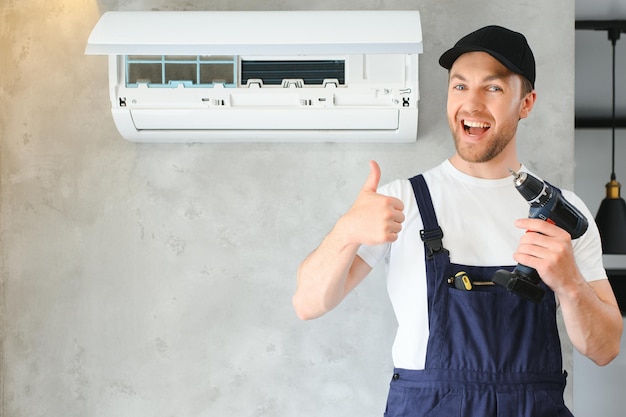 Lächelnder junger männlicher Elektriker repariert Klimaanlage im Haus des Kunden. Ein Mechaniker oder Mechaniker repariert Filter in der Klimaanlage im Haus des Kunden