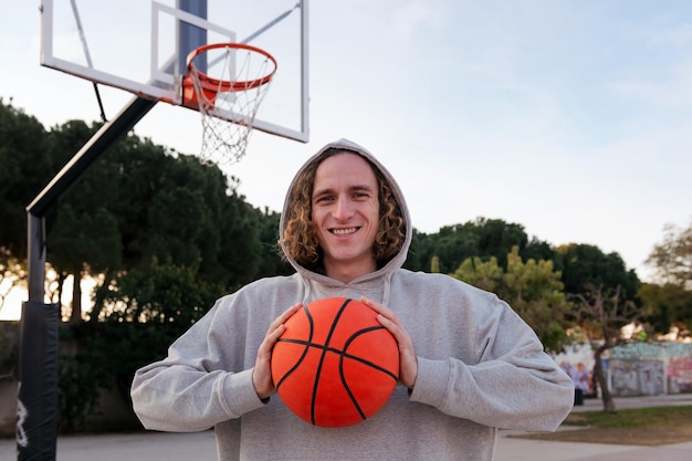 Lächelnder junger Mann auf einem Basketballplatz, der einen Ball in seinen Händen hält Konzept des städtischen Sports auf der Straße kopieren Platz für Text