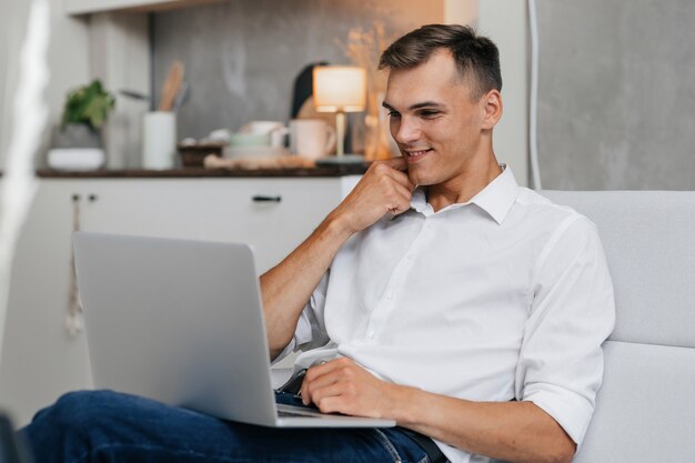 Lächelnder junger Mann, der auf den Bildschirm seines Laptops schaut
