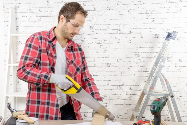 Lächelnder junger Mann, der ein Brett mit einer Handsäge schneidet