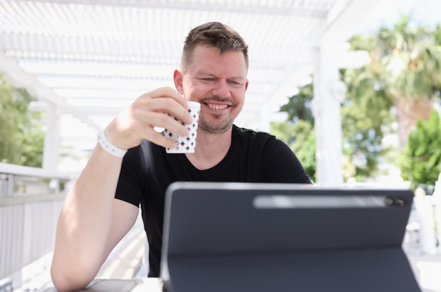 Lächelnder junger Mann, der mit einer Tasse Kaffee sitzt und auf der Straße an einem Tablet arbeitet?