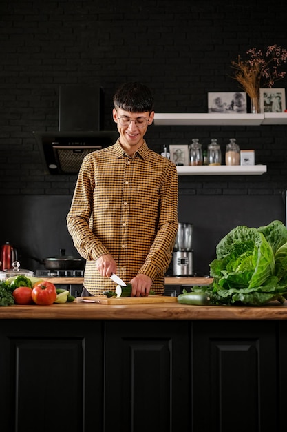 Lächelnder junger Mann, der Salat kocht, frisches Gemüse in moderner schwarzer Küche schneidet