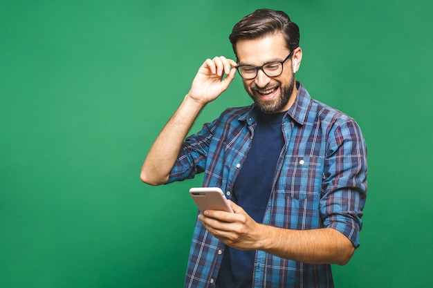 Lächelnder junger Mann, der Smartphone hält und es betrachtet. Porträt eines glücklichen Mannes unter Verwendung des Mobiltelefons lokalisiert über grünem Hintergrund.