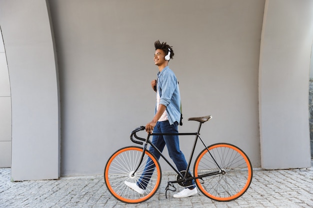 Lächelnder junger Mann draußen, mit dem Fahrrad gehend