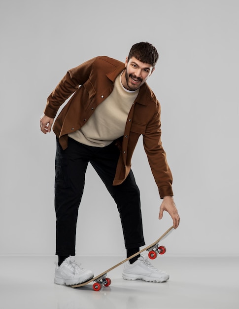 lächelnder junger Mann in brauner Jacke mit Skateboard