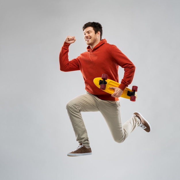 lächelnder junger Mann in Hoodie mit kurzem Skateboard