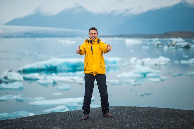 Lächelnder junger Mann mit Daumen nach oben in der Nähe der Gletscherlagune Jokulsarlon in Island