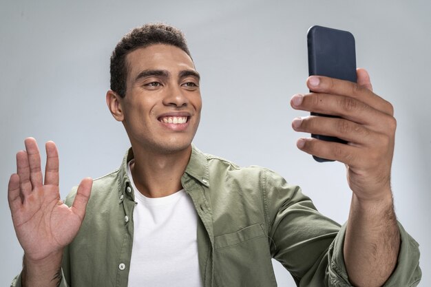 Lächelnder junger Mann winkt mit der Hand zu einem Smartphone-Bildschirm
