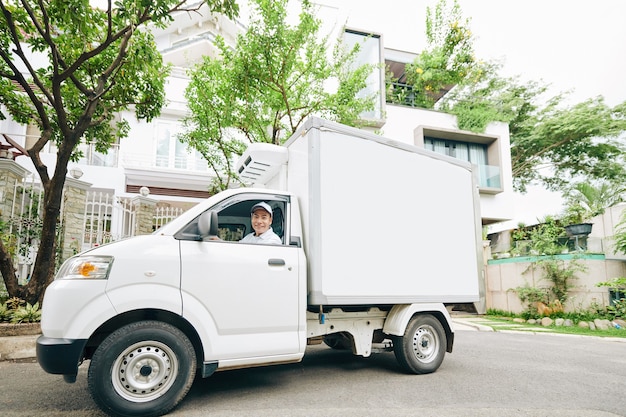 Lächelnder junger vietnamesischer Mann, der Milchwagen fährt und Milchprodukte liefert