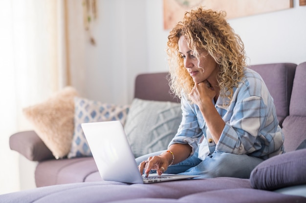 Lächelnder kaukasischer erwachsener Hipster sitzt entspannt auf der Couch und nutzt den modernen Laptop, der unbegrenzt surft