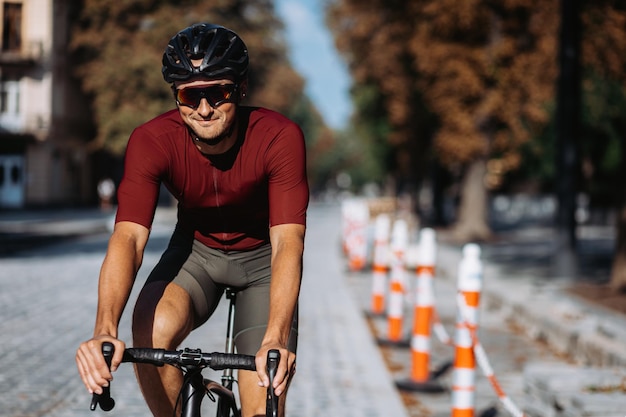 Lächelnder kaukasischer Mann mit Helm und Brille, der während der Reparaturarbeiten auf einem schwarzen Fahrrad auf der Stadtstraße fährt. Kaukasischer Sportler, der morgens Zeit für regelmäßiges Training an der frischen Luft verbringt.