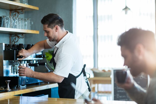 Lächelnder Kellner, der eine Tasse Kaffee macht