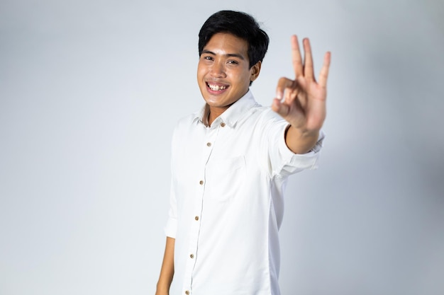 Lächelnder Kerl. Porträt eines aufgeregten und glücklichen jungen asiatischen Mannes, der OK-Zeichen auf grauem Hintergrund zeigt