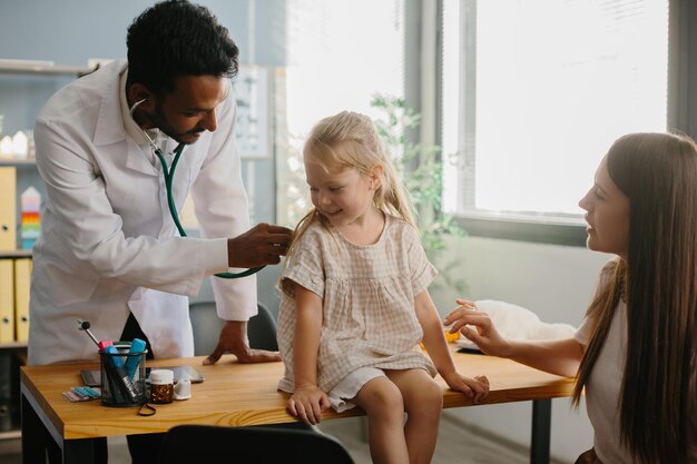 Lächelnder Kinderarzt mit Stethoskop überprüft die Lungen kleiner Mädchen