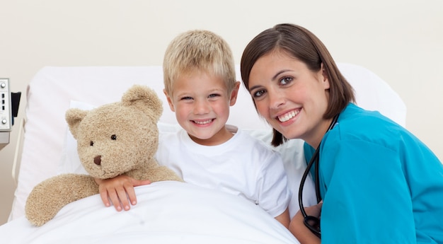 Lächelnder kleiner Junge und sein Doktor, die mit einem Teddybären spielen