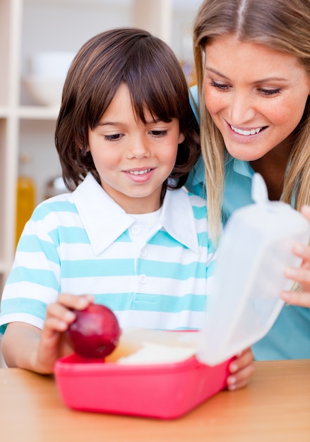 Lächelnder kleiner Junge und seine Mutter, die seinen Snack vorbereitet