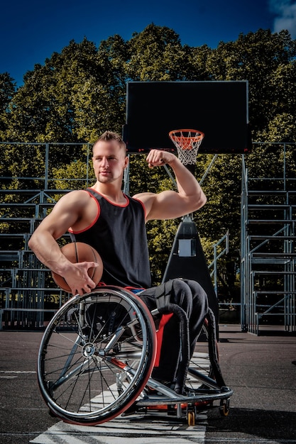 Lächelnder Krüppel-Basketballspieler im Rollstuhl hält einen Ball auf offenem Spielfeld.