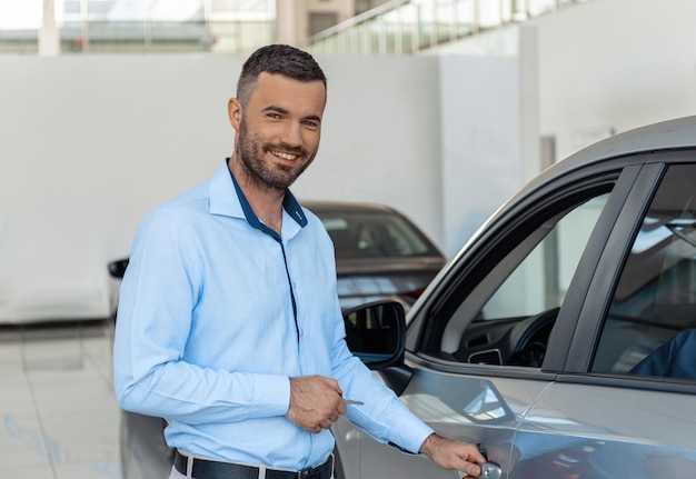 Lächelnder Kunde, der den Türknauf seines gerade gekauften Autos beim Händler öffnet