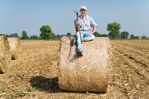 Lächelnder Landwirt, der auf einem Heuballen auf seinem Gebiet sitzt