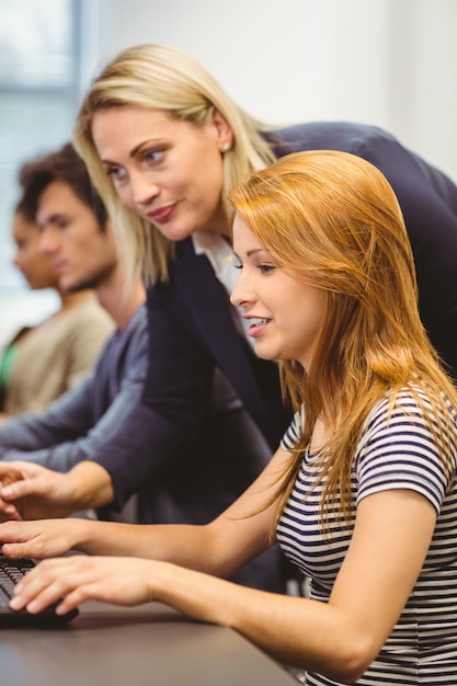 Foto lächelnder lehrer, der dem studenten im computerraum etwas erklärt