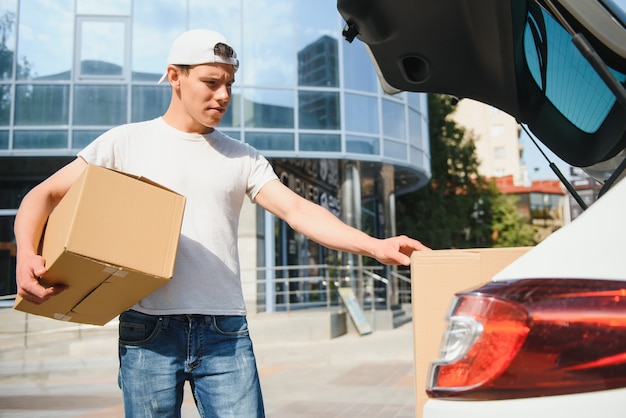 Lächelnder Lieferbote, der vor seinem Auto steht