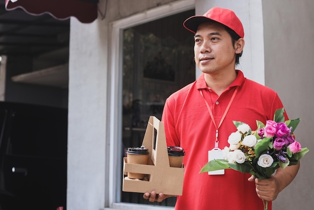 Lächelnder Lieferbote hält einen schönen Blumenstrauß und Kaffeetassen bereit, um ihn an den Kunden zu liefern