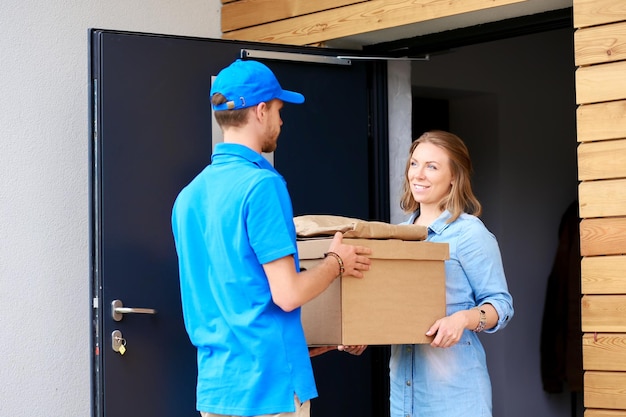 Lächelnder Lieferbote in blauer Uniform, der Paketbox an das Kurierdienstkonzept des Empfängers liefert Lächelnder Lieferbote in blauer Uniform